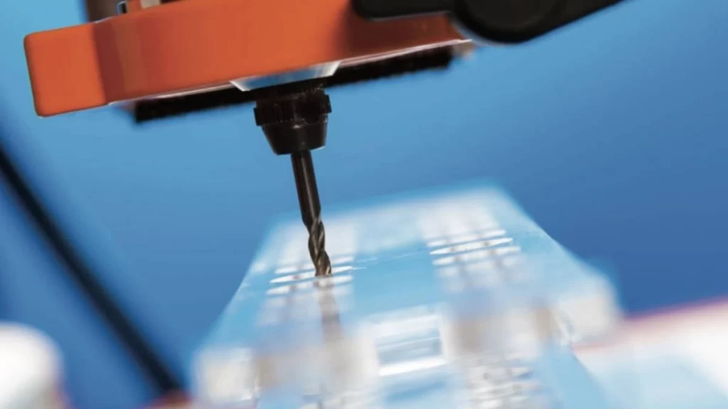 A CNC drill shaping holes in a clear acrylic (PMMA) sheet