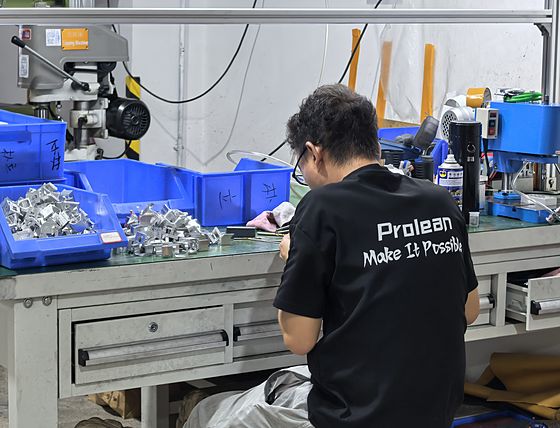 Ein Mitarbeiter in einem Proleantech-Arbeitshemd sortiert an einer Werkbank bearbeitete Teile in blaue Behälter.